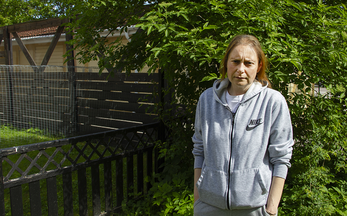 Halvkroppsporträtt på Antonia Giaretta, som står i en grå huvtröja med uppkavlade ärmar och långt brunt hår i tofs framför staketet till sin uteplats. Hon har ett nätstaket åt ena hållet för katternas skull och ett plank mot förråden.