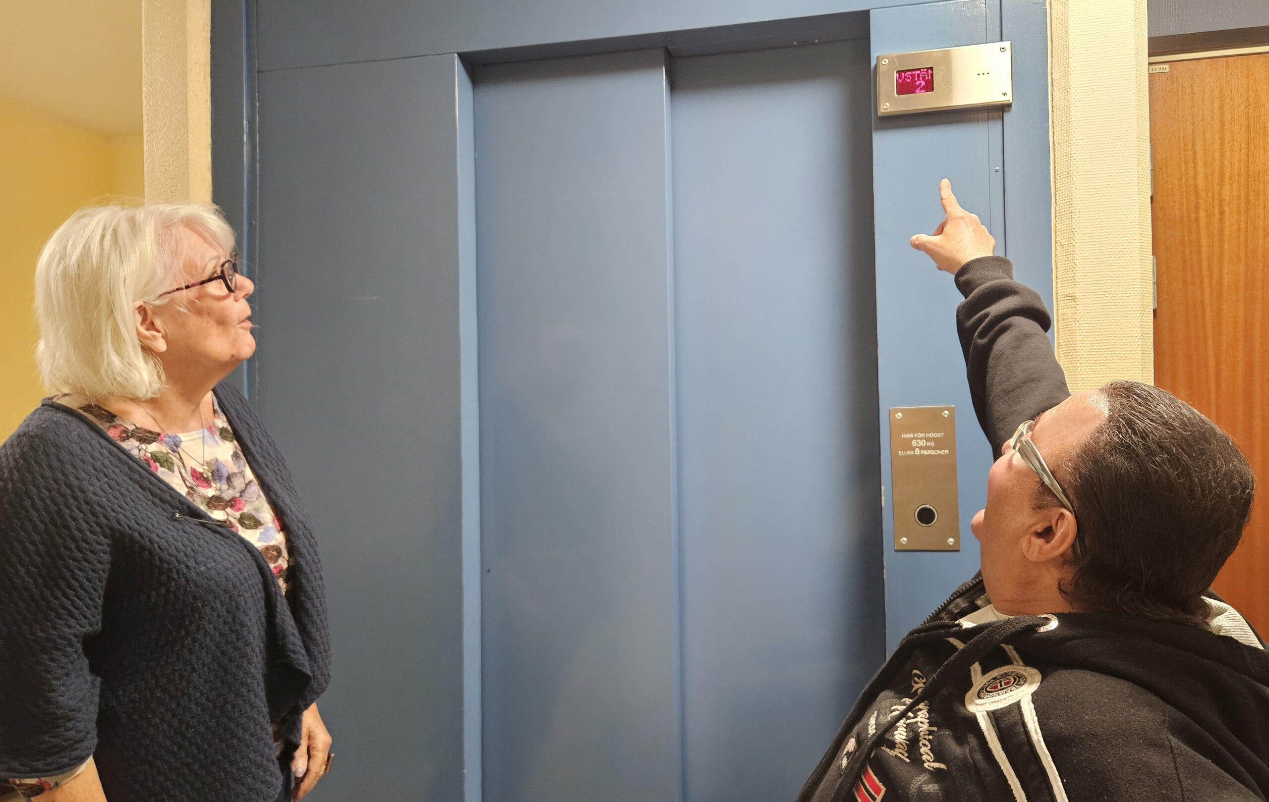Två personer vid en hissdörr.
