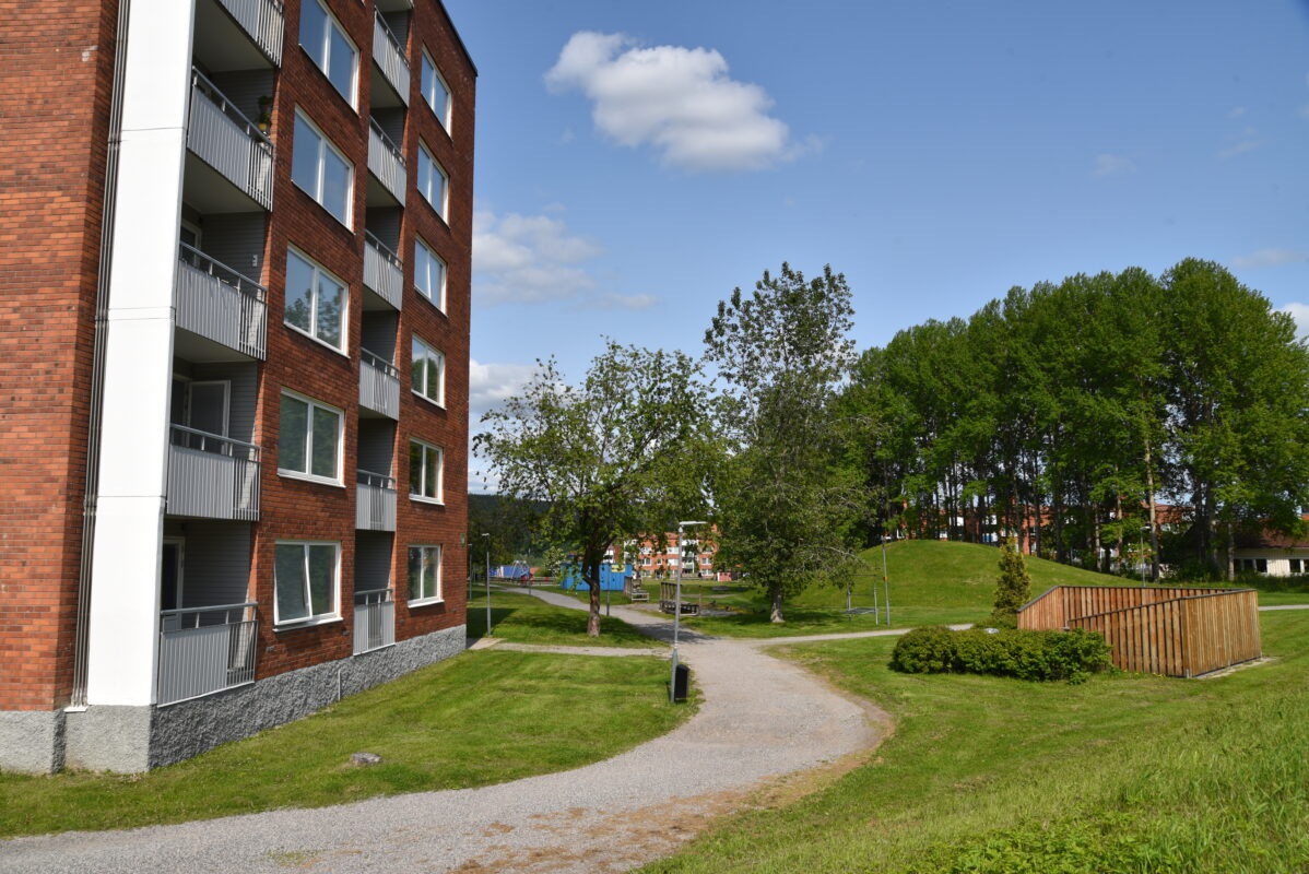 bilden visar en del av ett höghus i tegel, en blå himmel och gröna kullar.