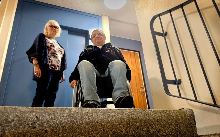 En kvinna och en man vid en trapp och i bakgrunden en blå hissdörr.