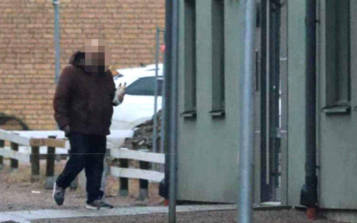 En man utanför ett bostadshus som håller en korv i handen. Mannens ansikte är pixlat.