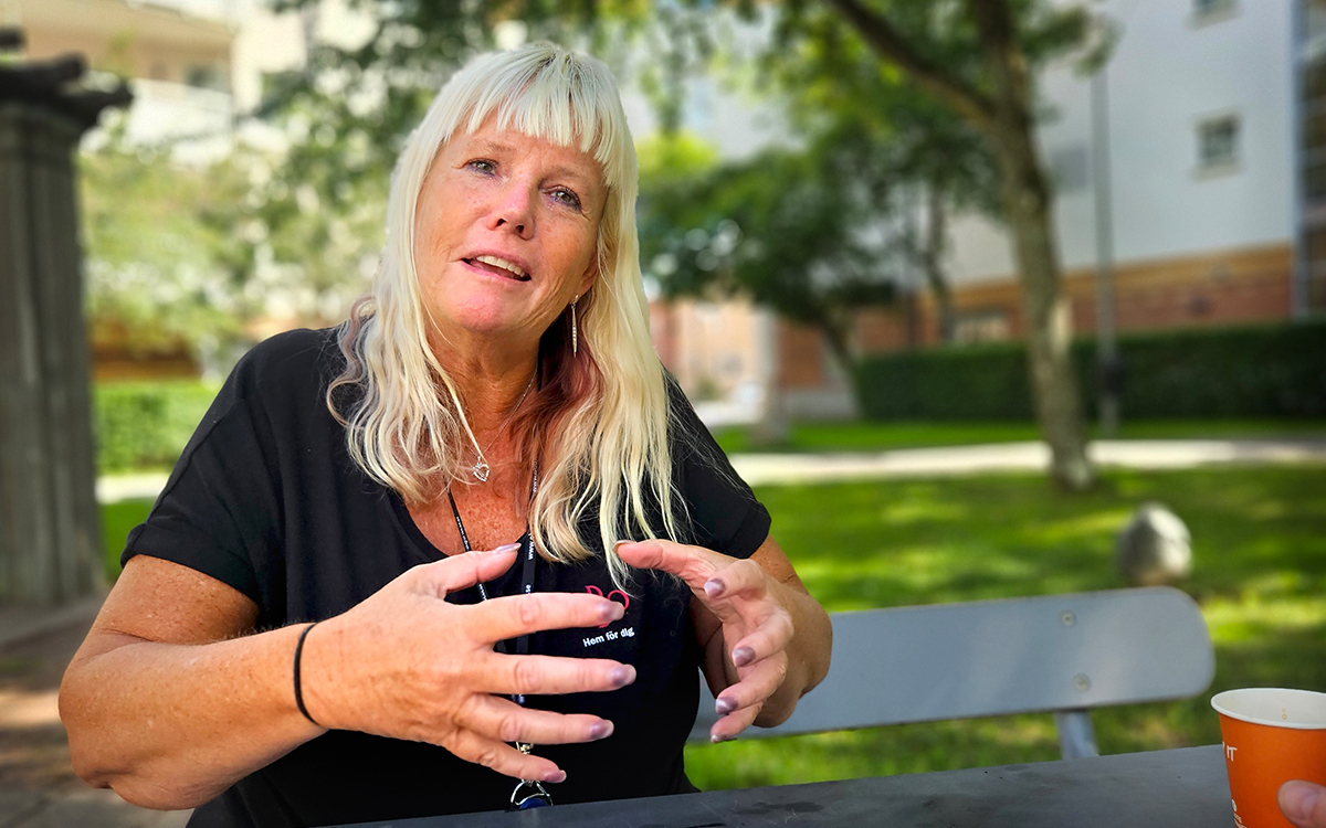 Kvinna i en trädgårdsmiljö. Halvfigur. Hon gestikulerar med händerna och tittar in i kameran.
