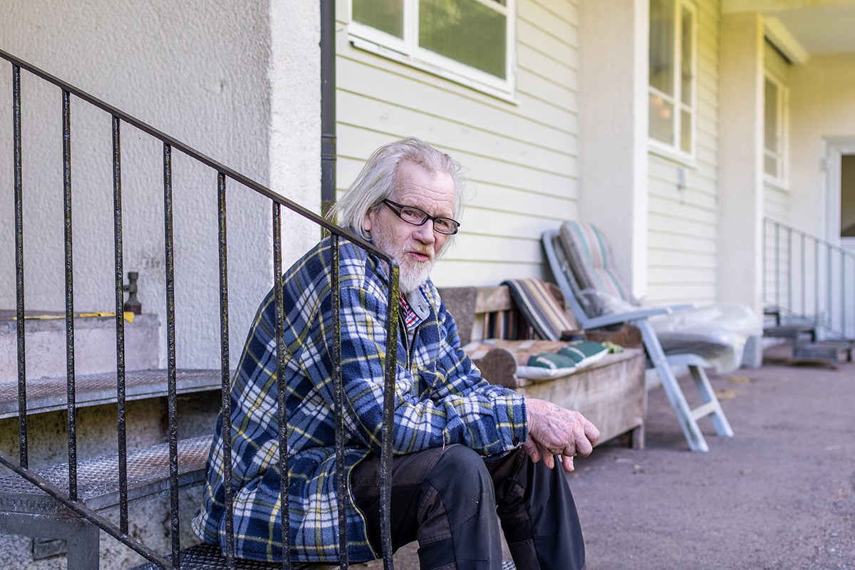 En man som sitter på en trappa. Han har skägg och en rutig skjorta.