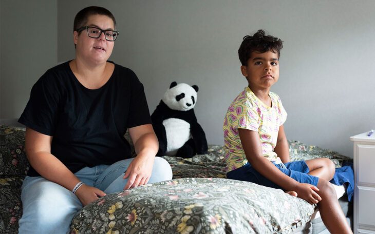 En ung kvinna i kort hår och glasögon som sitter på en säng med en liten pojke.