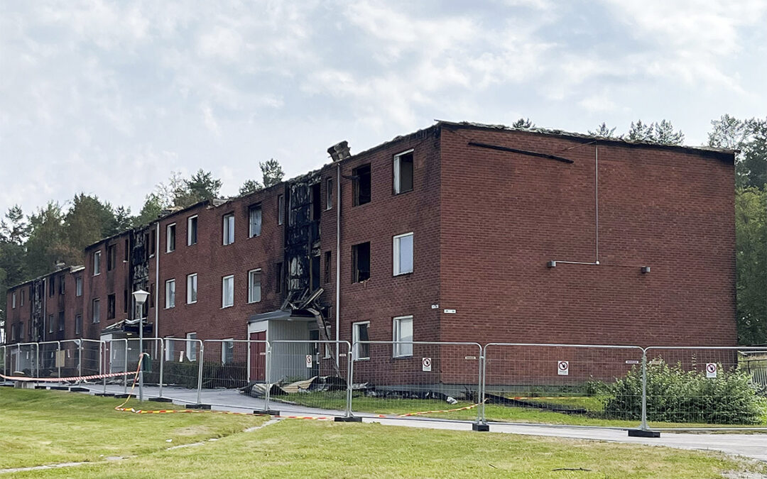 Ett trevåningshus i tegel med tydliga skador av brand i form av sot, delar av taket på marken och saknade fönster. Runt byggnaden ett byggarbetsplatsstaket. Glada Hudikhems vd Stefan Söderlund lovar att alla hyresgäster som drabbades av branden som behöver det ska erbjudas permanenta hyreskontrakt.