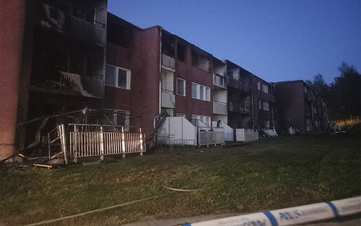 Foto på ett tegelhus i tre våningar med spår efter en kraftig brand. Fotot är taget när det är mörkt ute. I förgrunden syns ett polisavspärrningsband. Hyresgäster i 36 lägenheter förlorade sina hem vid branden på Stormyravägen. Hyresgästföreningen var snabbt på plats för att stötta de drabbade hyresgästerna.