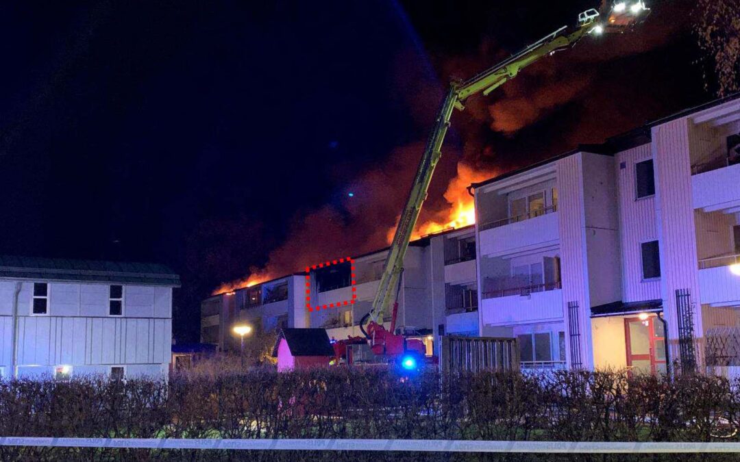 Bilden föreställer räddningsarbetet vid ett brinnande hus, i mörkret på kvällen. En balkong är markerad med rött. Där började branden.
