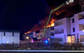 Bilden föreställer räddningsarbetet vid ett brinnande hus, i mörkret på kvällen. En balkong är markerad med rött. Där började branden.