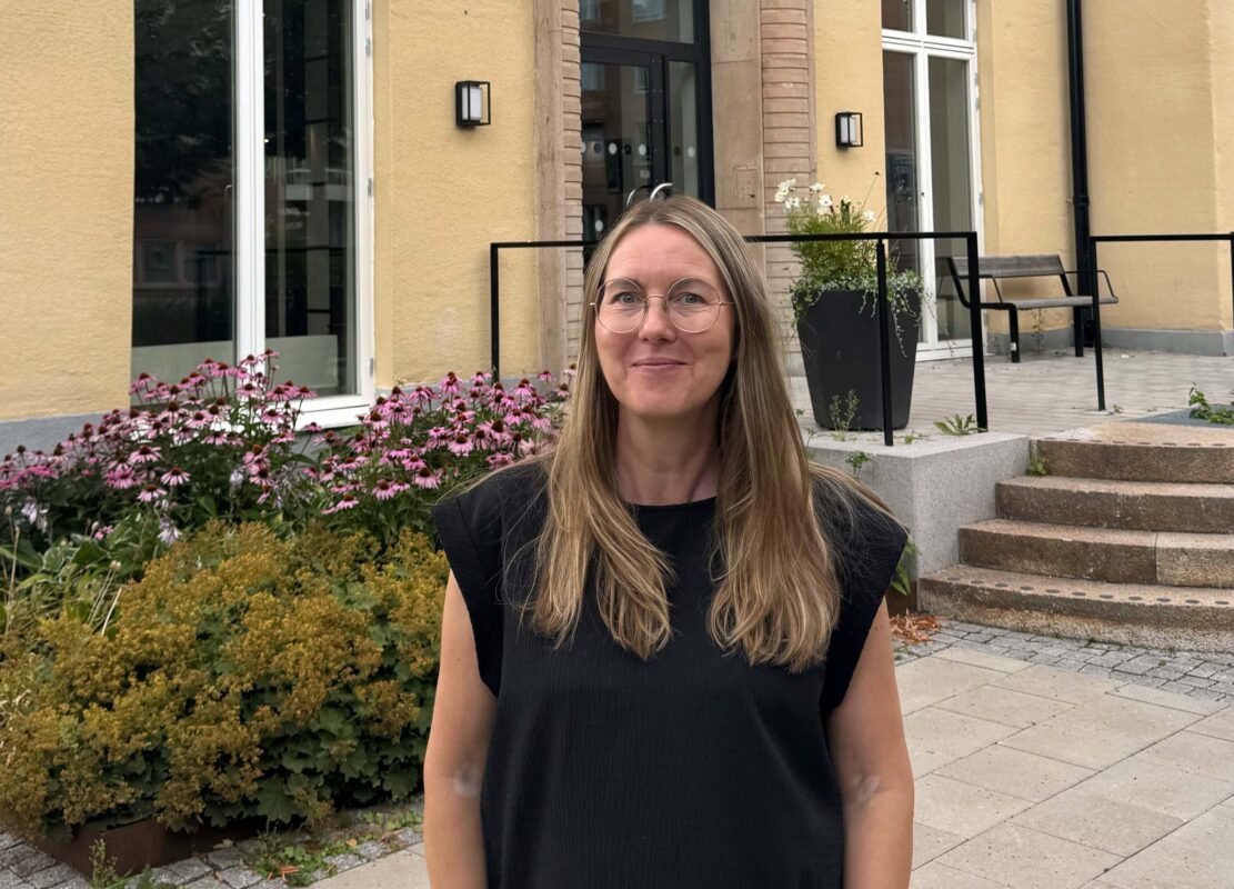 En svartklädd kvinna med långt mellanblont hår och glasögon står framför en byggnad som det står Uppsalahem på.