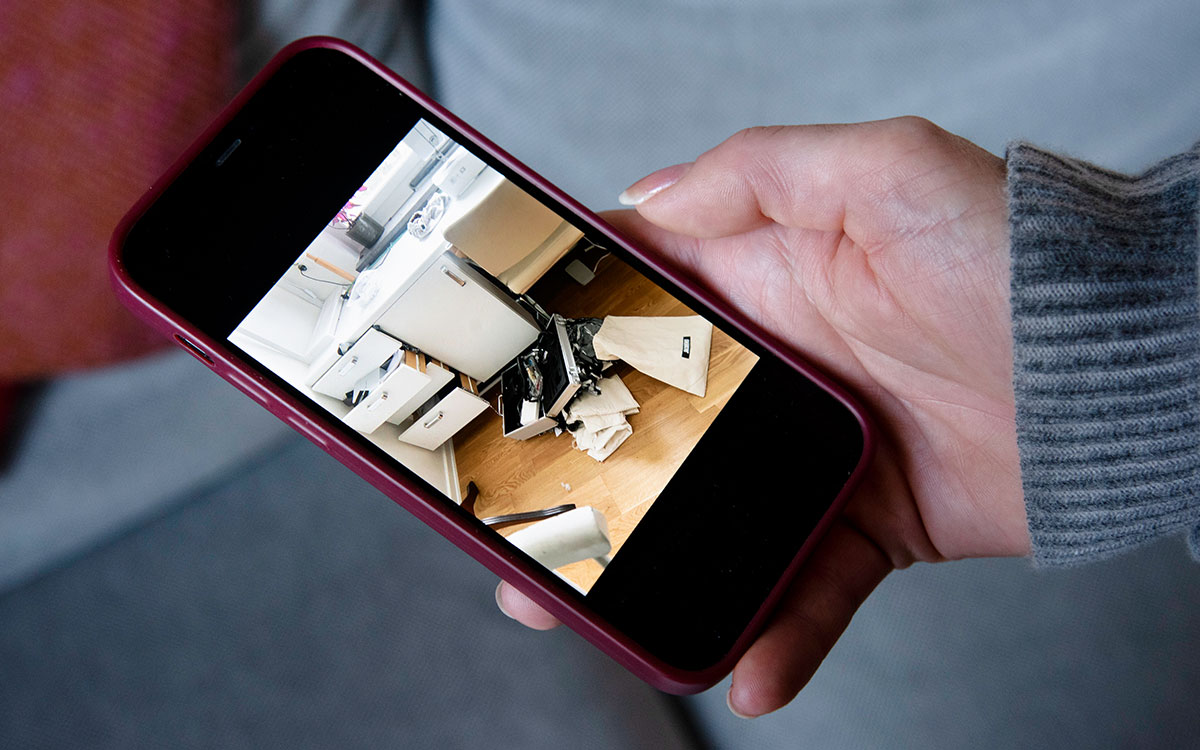 Hand med mobil som visar bild på hur det såg ut efter inbrott.