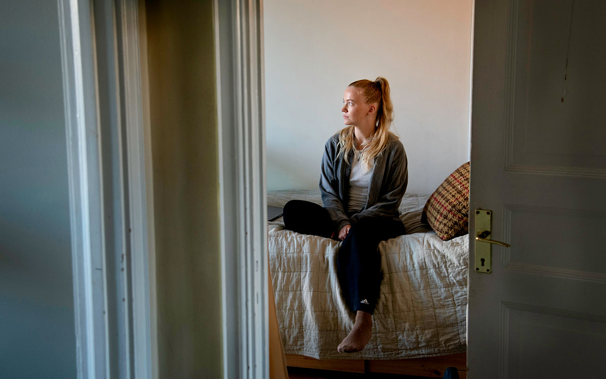 Alva sitter på sängen och tittar åt sidan.