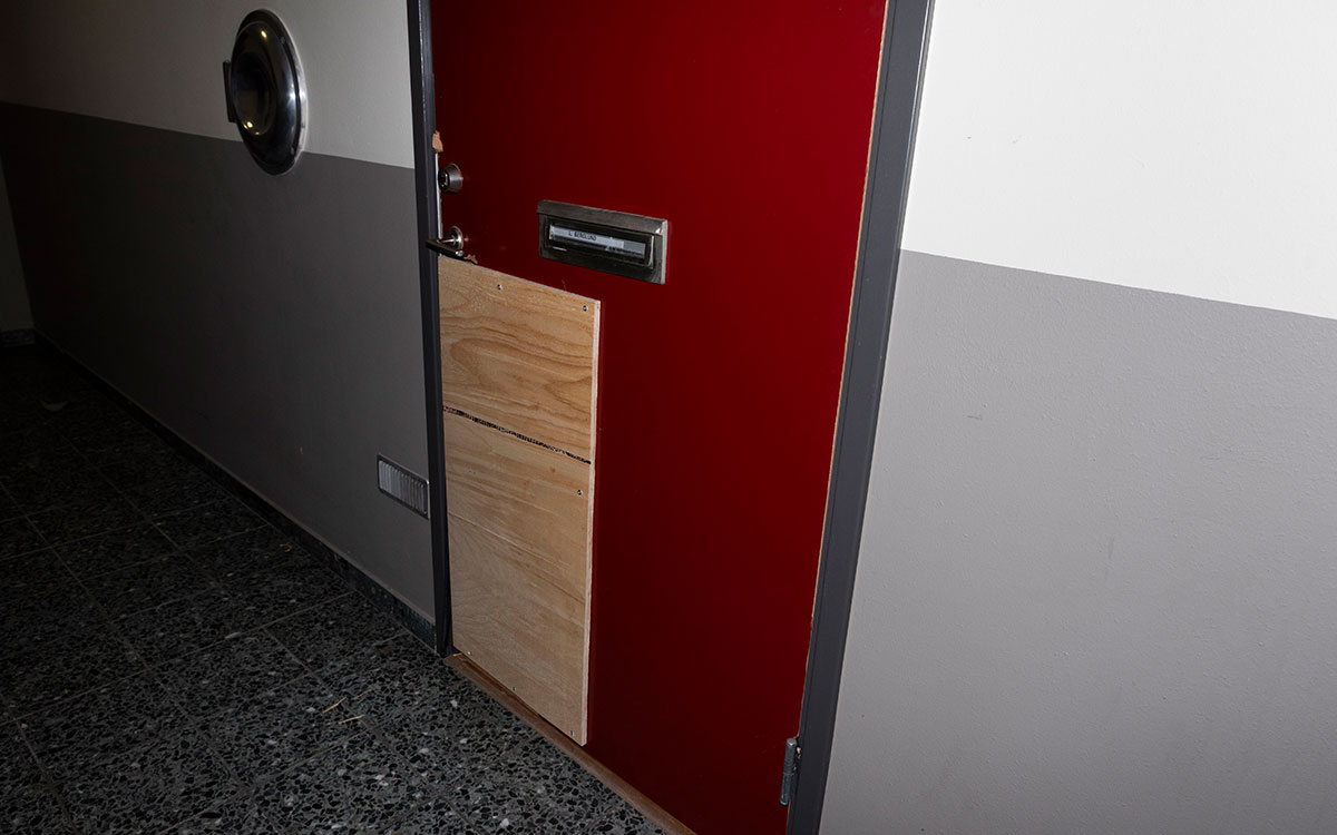 En röd dörr i ett trapphus där den nedre delen satts för med en obehandlad träskiva.