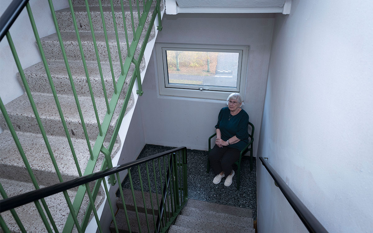 En äldre kvinna som sitter på en stol i ett trapphus.