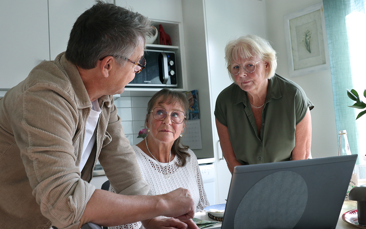 En man vid en dator som tittar mot två kvinnor. De är i ett kök.