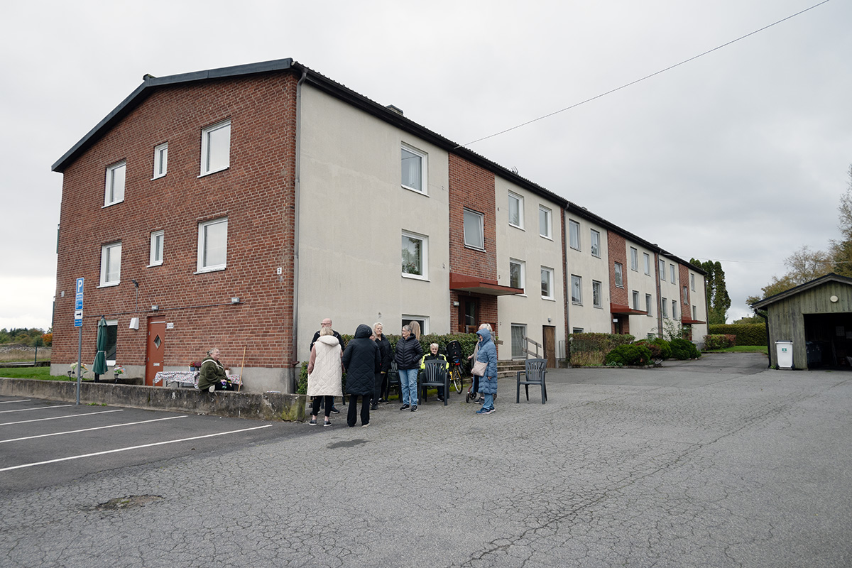Ett flervåningshus. Framför en grupp med personer.