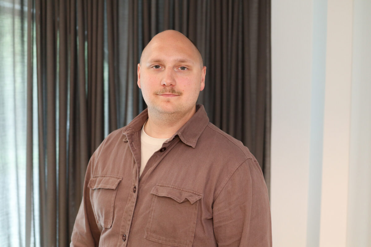 En man med mustasch tittar in i kameran. Neutralt uttryck.