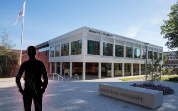 Svart silhuett av en man. I bakgrunden en vit, modern byggnad med stora fönster.