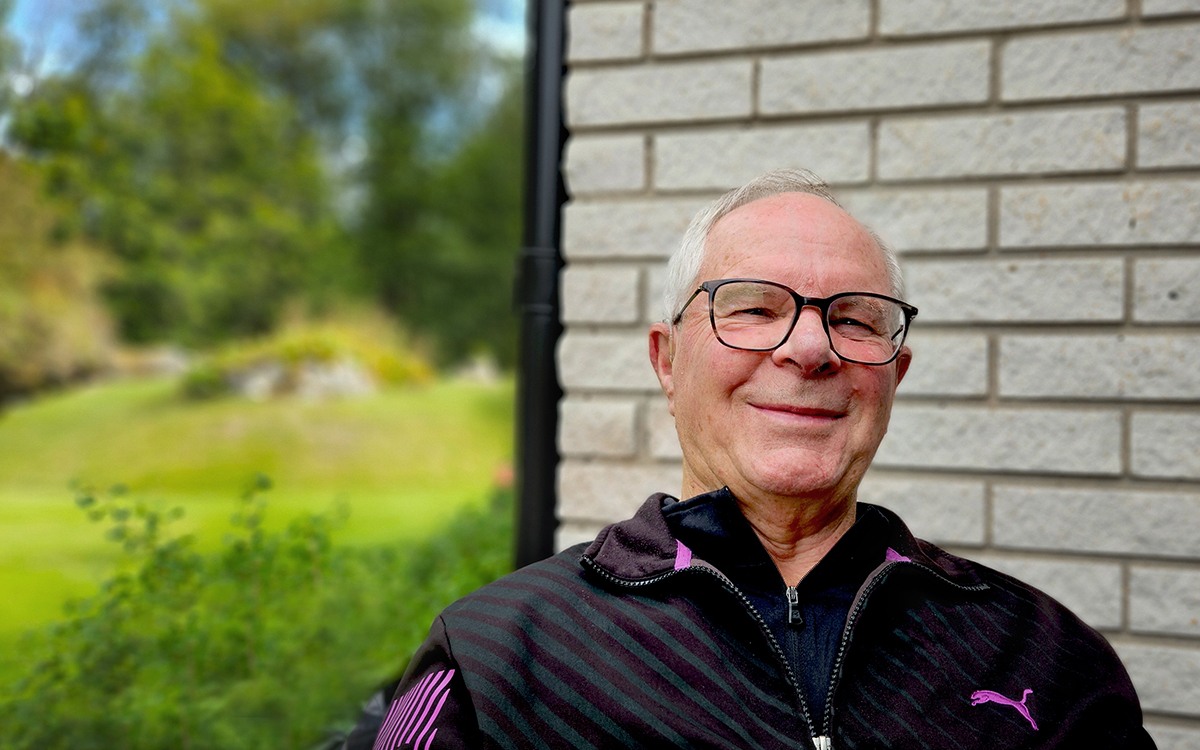 Man som sitter ner. han tittar in i kameran och ler. Bakom honom syns en vit vägg i tegel.