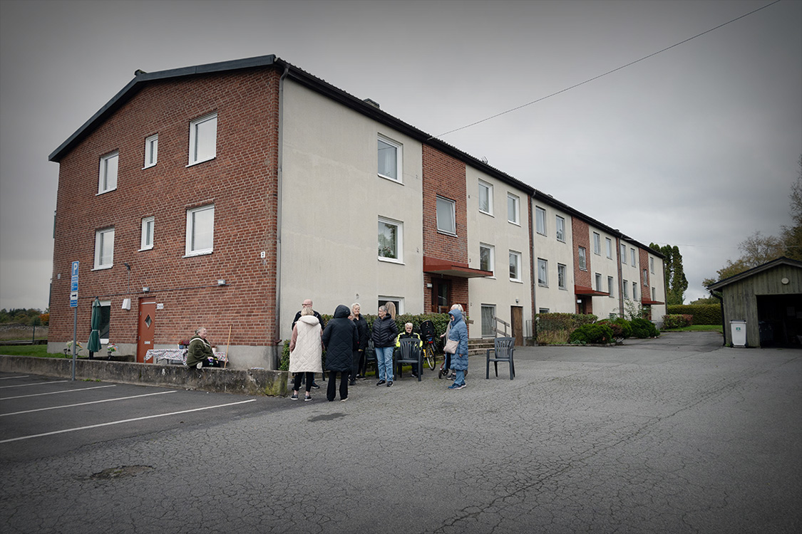 Ett flerfamiljshus med en grupp människor framför.