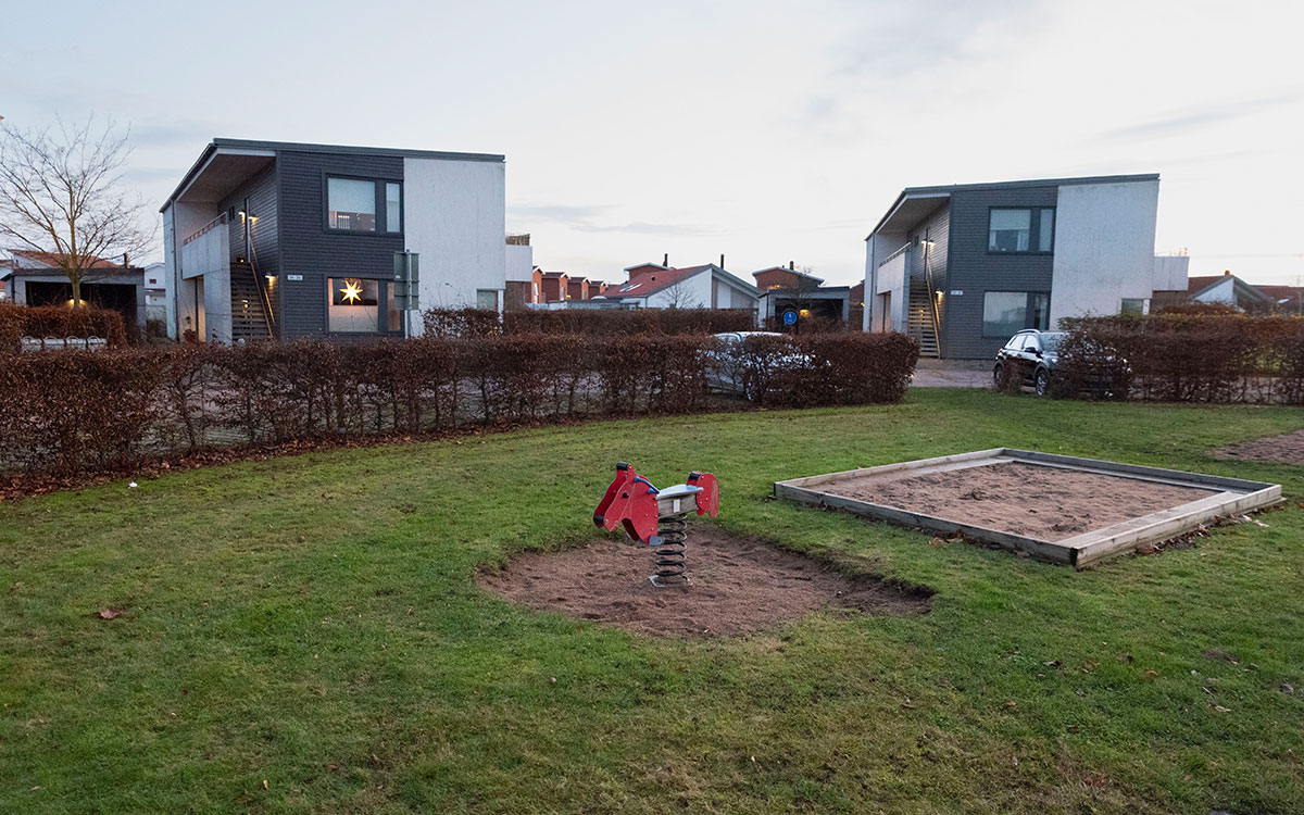 Vita hus med platta tak i två våningar bakom en gräsmatta med ett lekredskap i form av en röd älg eller häst.