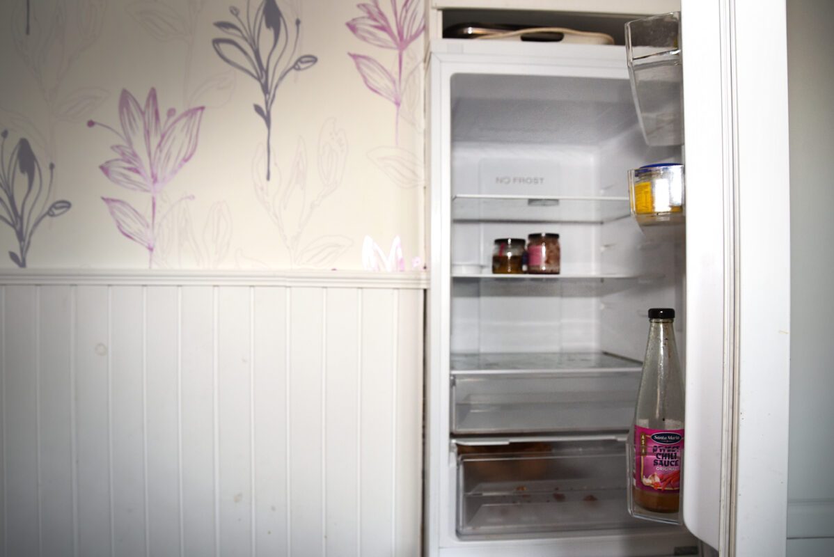 Ett kylskåp som står öppet. Det är avstängt och det står bara några flaskor och burkar som inte kräver kyla där inuti.