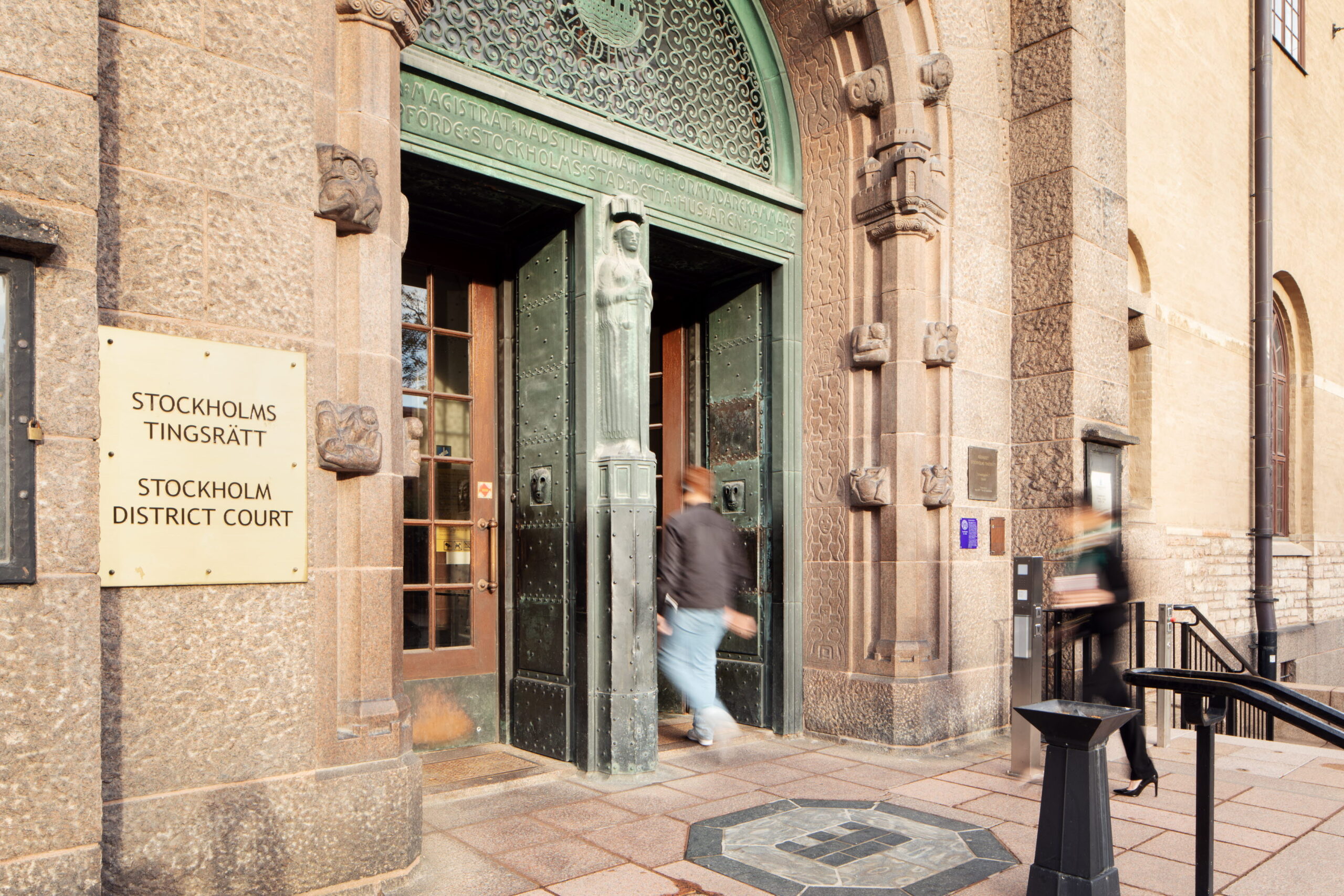Foto på Stockholms tingsrätts entré i rödaktig sten + grönärgad koppar med utsmyckningar ovanför och runt om dörrparet, två dörrar i koppar. En person i rörelseoskärpa är på väg in genom den högra dörren. Till vänster en skylt med "Stockholms tingsrätt Stockholm district court" i versaler. Olika företag har i en rad fall vänt sig till tingsrätten för att kräva pengar av Annika Backlund och AB-hem.