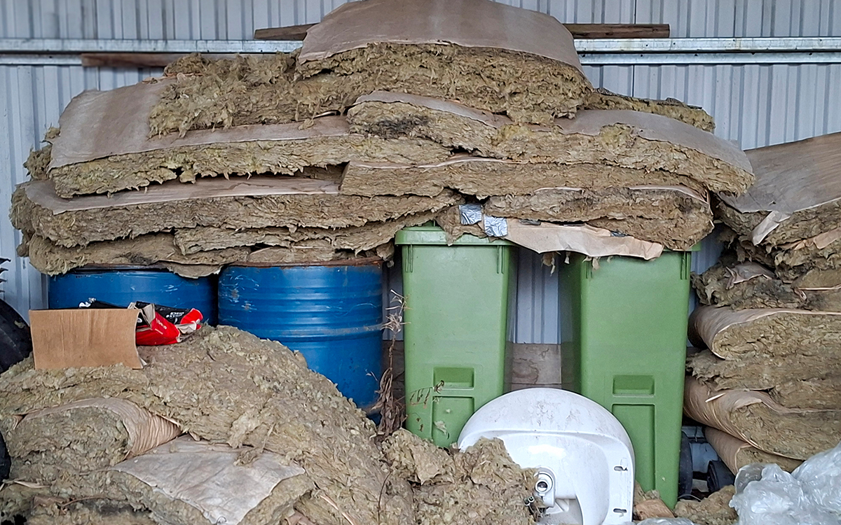 Bild som visar oljetunnor och sopkärl. Framför och ovanpå ligger gammal isolering.