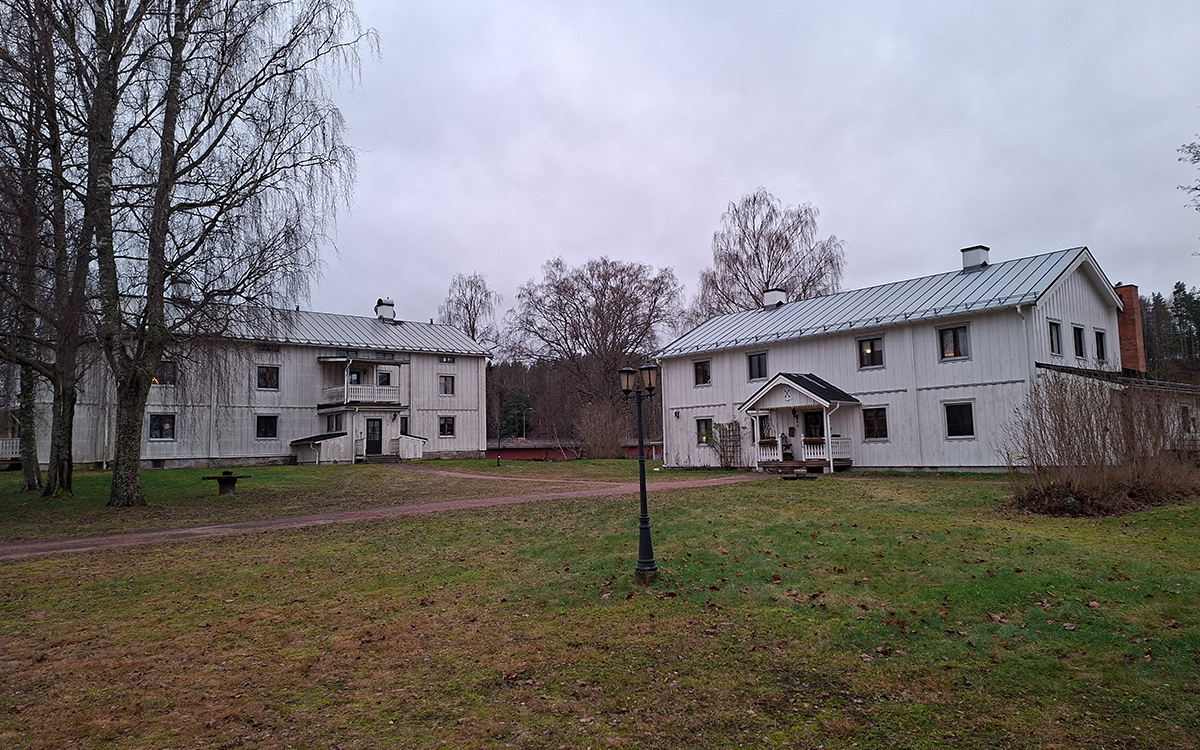 Bilden visar två vita trähus. Gräsmatta i förgrunden.