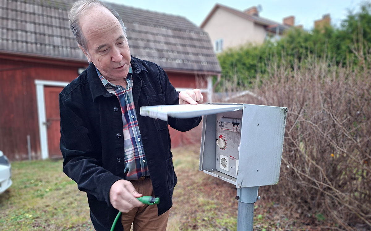 En man som står bredvid en motorvärmarstolpe. Han håller en sladd i ena handen.