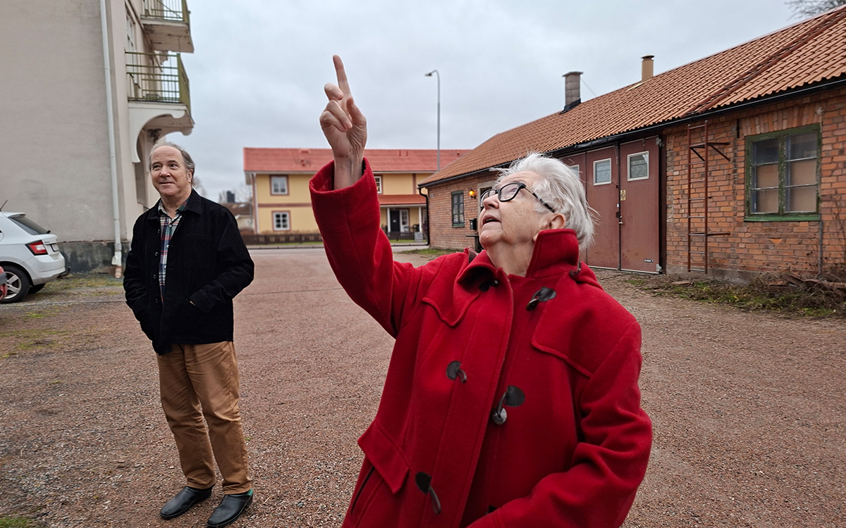 Kvinna som pekar upp i luften. I bakgrunden syns en man som tittar på henne. De står på en gård.