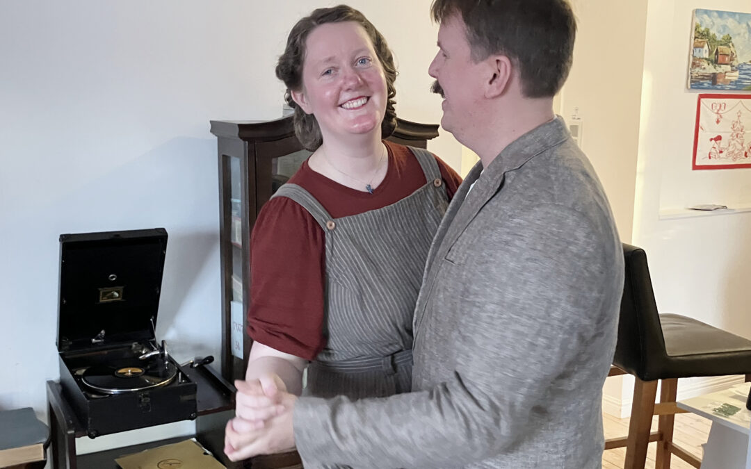 Ett par runt 30 dansar i ett vardagsrum. I bakgrunden en vevgrammofon. De håller varandra i händerna i styrdans. Hon tittar in i kameran, han syns i profil. Hon har vinröd t-shirt och hängselbyxor. Han har mustasch och ljus kavaj.