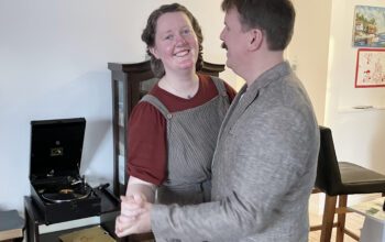 Ett par runt 30 dansar i ett vardagsrum. I bakgrunden en vevgrammofon. De håller varandra i händerna i styrdans. Hon tittar in i kameran, han syns i profil. Hon har vinröd t-shirt och hängselbyxor. Han har mustasch och ljus kavaj.