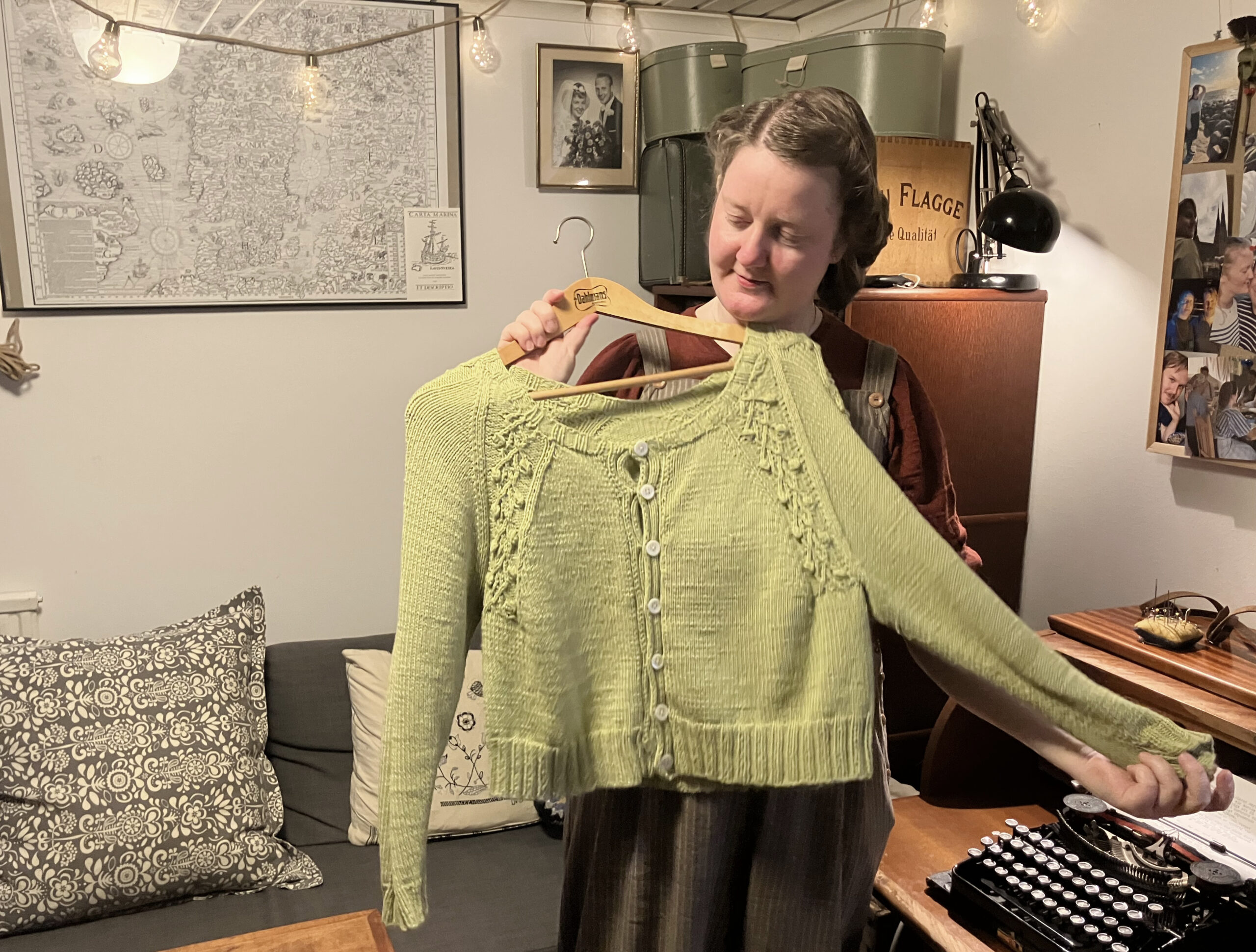 En kvinna i håruppsättning à la 40-tal håller upp en limegrön stickad kofta mot kameran.