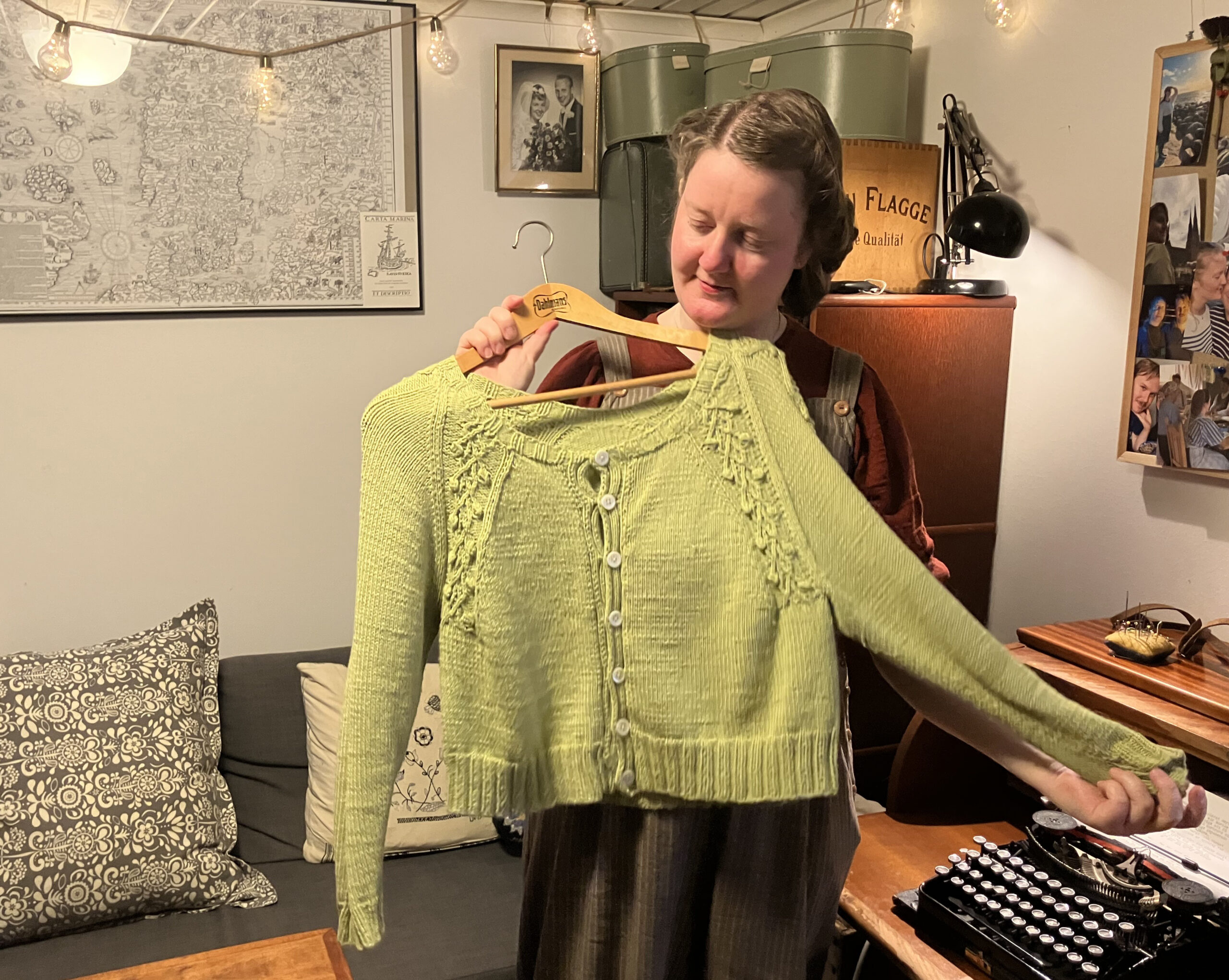 Kvinna med håruppsättning a la 40-tal håller upp en hemstickad limegrön kofta mot kameran.