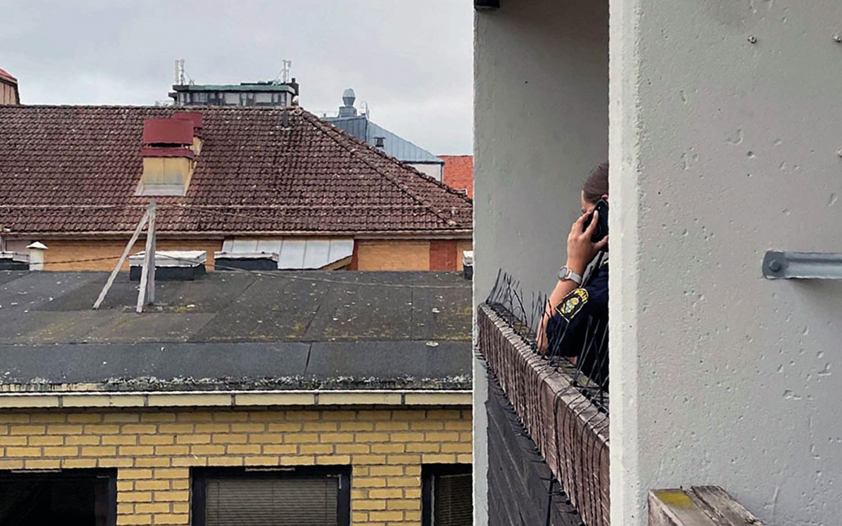 En polis som tittar ut från en balkong mot innergården på Hantverkaregatan.