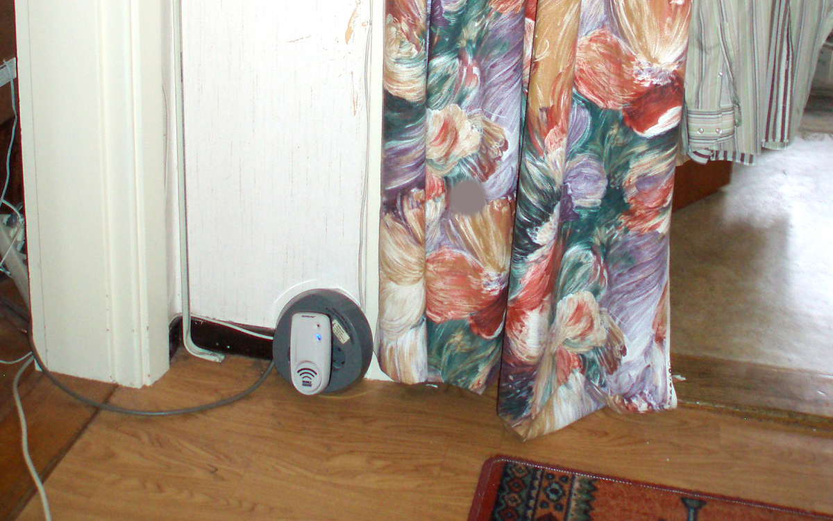 Bilden visar en musskrämma som är inpluggad i ett grenuttag. I bakgrunden syns en vit vägg och ett blommigt draperi.