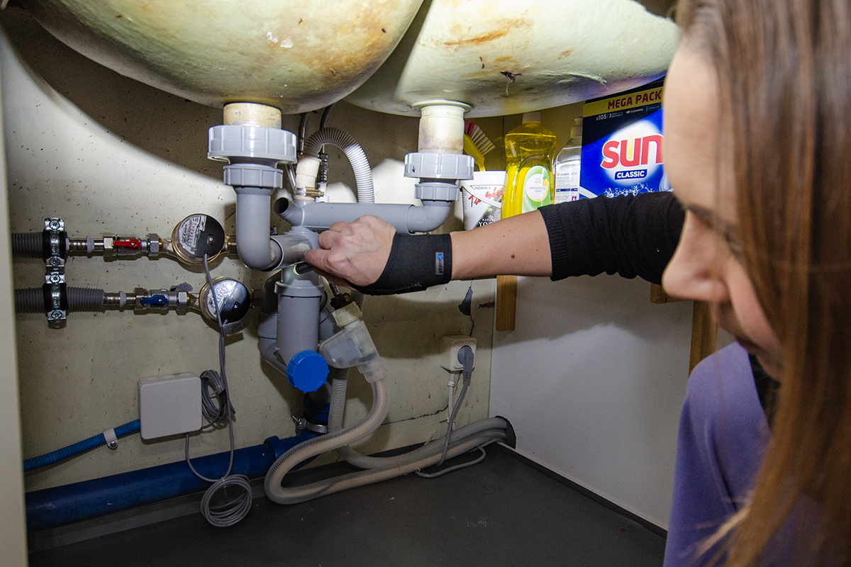 Marlene Rydell lyser med ficklampa på de runda mätarna, en för varmvatten och en för kallvatten, som läser av hur mycket vatten som går ut i kökskranen.