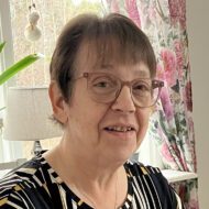 Porträttbild på kvinna 60 plus. Hon har kortklippt mörkt hår, glasögon och ler lätt in i kameran.