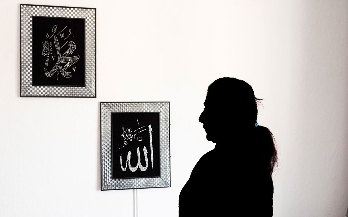 En kvinna i siluett framför en vägg med tavlor med arabisk skrift där det står Allah och Mohammed.