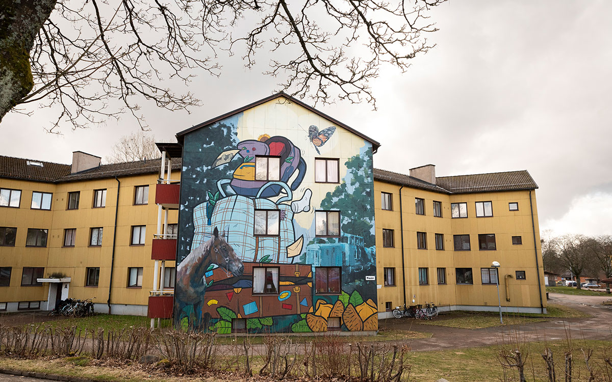 Ett gult flervåningshus med en muralmålning på en fasad.