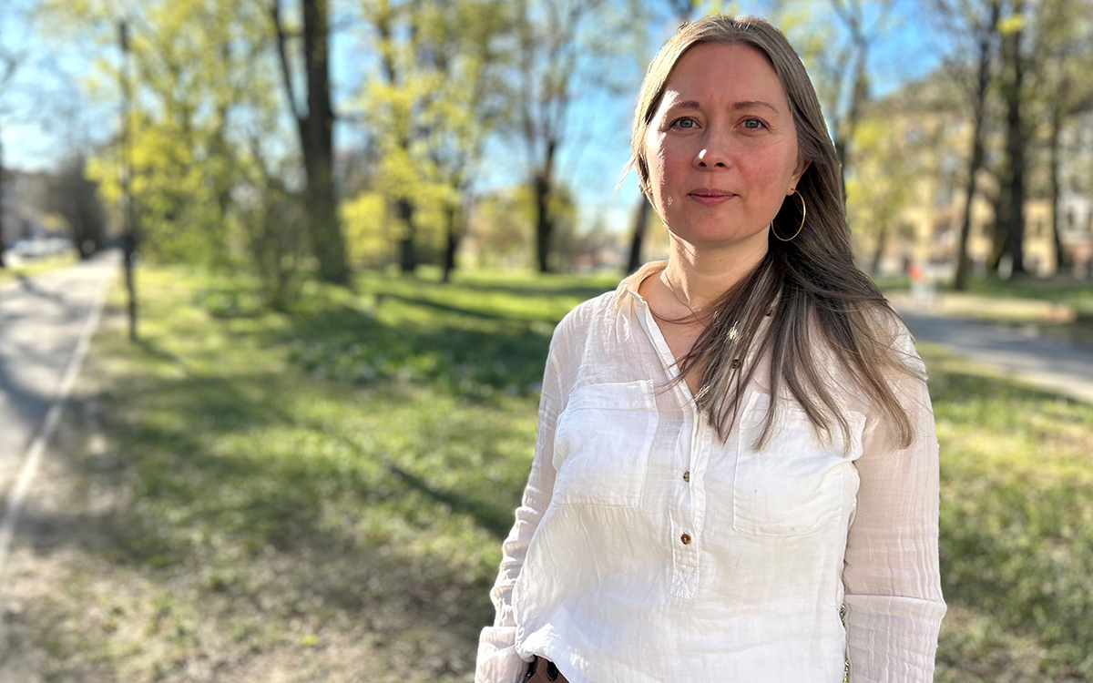 Kvinna i halvfigur. I bakgrunden syns en park.