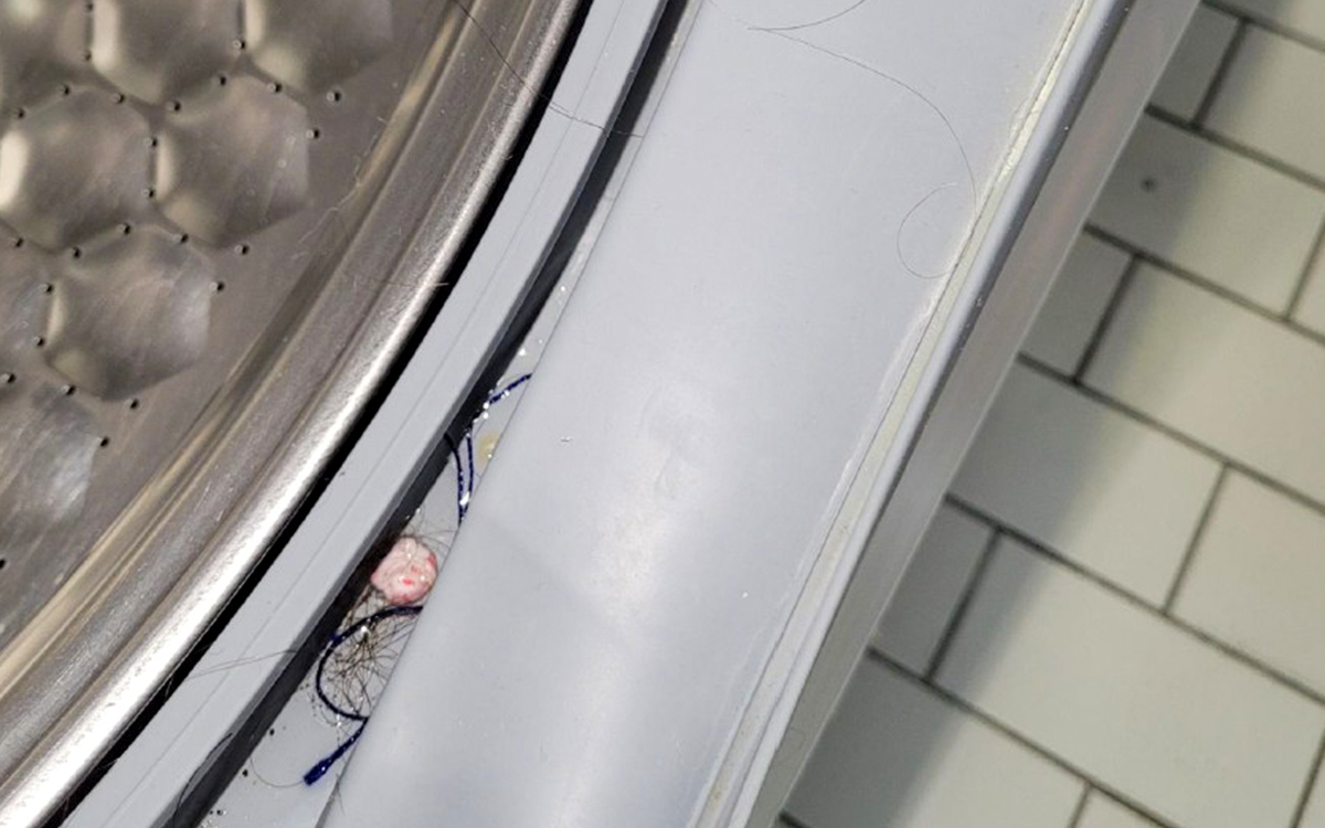 Bilden visar en del av en tvättrumma där man ser hårstrån och skräp ligga kvar.