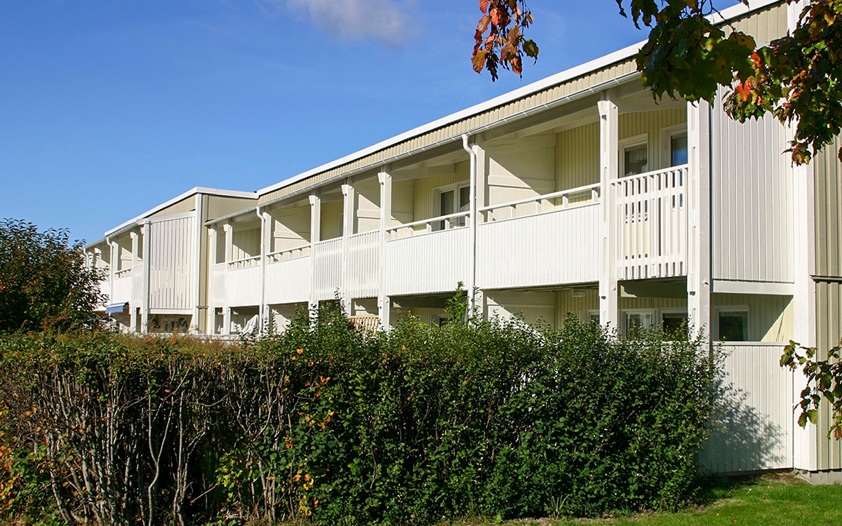 Vit radhuslänga i två våningar där man mest ser den översta våningen. I förgrunden syns en häck. 