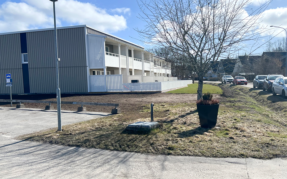 Bild på en radhuslänga. Ett lågt vitt staket avgränsar uteplatserna. Därefter ses en gräsmatta