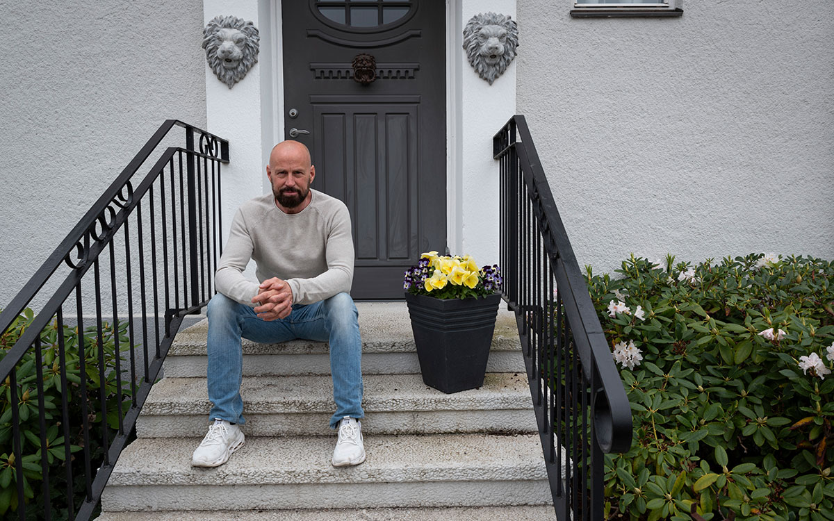 En skäggig skallig man iklädd jeans och tröja sitter på trappan utanför, och fasaden är dekorerad med lejonmakron.