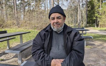 En bild på en man i 70-årsåldern. Han sitter vid ett träbord ute med en skog i bakgrunden. Han har svart mössa, lite skäggväxt och har händerna knäppta framför sig. han tittar allvarligt in i kameran. Han har svart mössa, svart jacka och grå tröja. Uppsalahem har infört en tipsfunktion för att komma åt otillåten andrahandsuthyrning.
