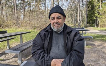 En bild på en man i 70-årsåldern. Han sitter vid ett träbord ute med en skog i bakgrunden. Han har svart mössa, lite skäggväxt och har händerna knäppta framför sig. han tittar allvarligt in i kameran. Han har svart mössa, svart jacka och grå tröja. Uppsalahem har infört en tipsfunktion för att komma åt otillåten andrahandsuthyrning.