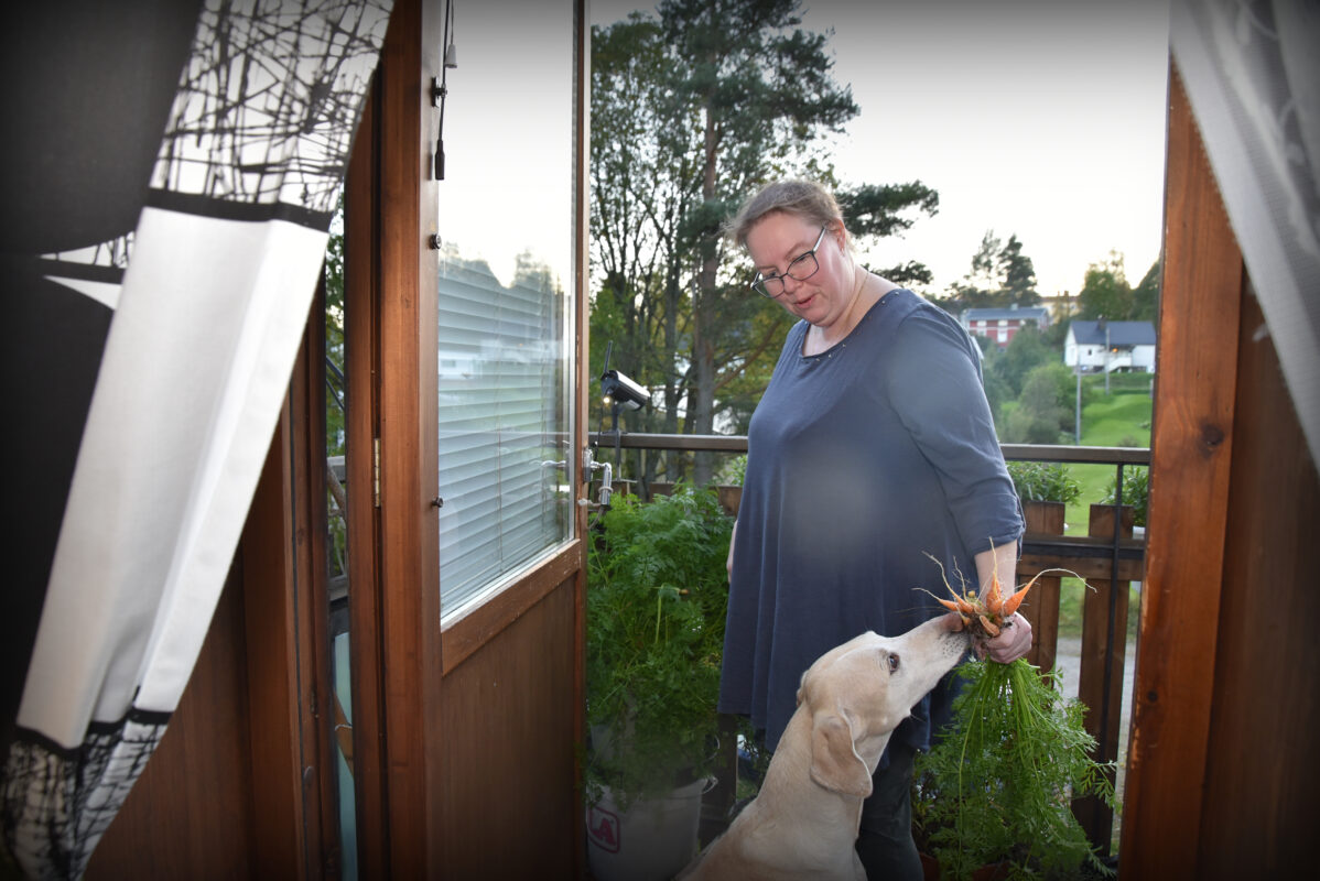 En hund som nosar på morötter ute på en balkong, tillsammans med sin matte.