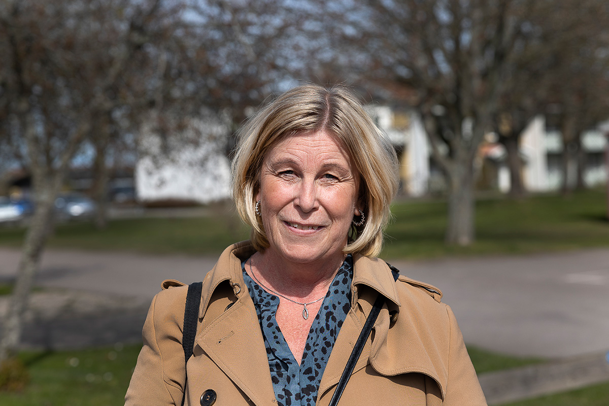 En kvinna i beige kappa och kort ljust hår som tittar rakt fram.