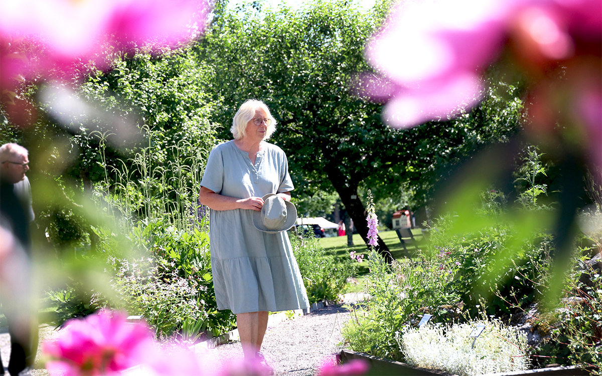Kvinna i helfigur. Fotograferad lite på håll och bilden omramas av rosa blommor. Skärpan ligger på kvinnan.